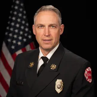 Man in suit with Saint Paul Fire Department badge and lapel pins poses for portrait in front of an American flag.