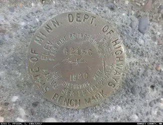 Close-up of an aluminum bridge disk, with "State of Minn. Department of Highways Bench Mark" stamped into it.