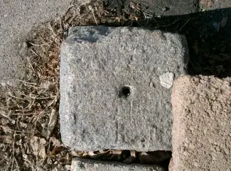 Top view of a square block of granite with a hole drilled in the center.