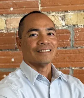 A man smiles for a portrait in front of a brick wall