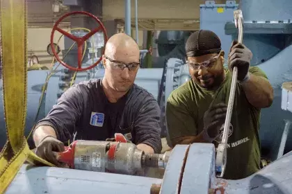 Two men installing a large diameter nut and bolt onto a water pump