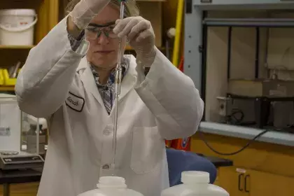 Woman using pipette to transfer water between two plastic bottles on a laboratory bench