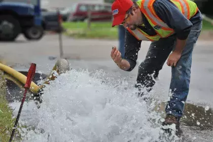 Man collecting water sample from a pipe that is openly flowing water into the stree