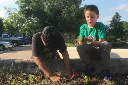 Two boys planting: One boy stands beside a raised garden bed while another sits inside