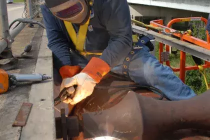 Person welding on the side of a bridge