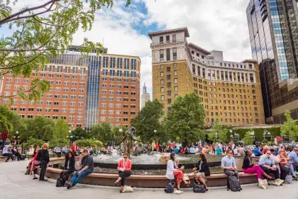 A crowd of people sits around a circular fountain in downtown Saint Paul talking and eating lunch.