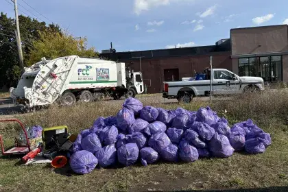 Pile of garbage bags in a field post litter cleanup with St Paul and FCC truck in the background