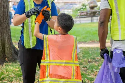 A picture of a litter cleanup volunteer helping a younger volunteer put their gloves on
