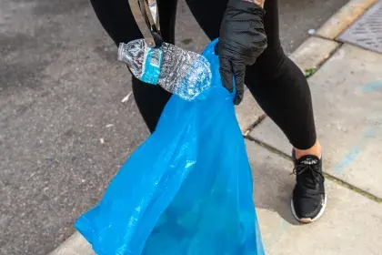 Litter volunteer picking up a water bottle with a litter grabber and recycling it 