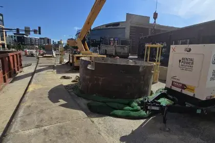 Photo showing large metal round frame in street with construction crane in background as part of sewer construction on West 7th Street in Saint Paul. For accessibility call 651-266-6100.