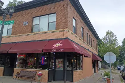Two Scoops Ice Cream Eatery at 921 W. Selby Avenue, a two-story brick corner building with maroon awnings, a red "Open" neon sign and a black bench outside.