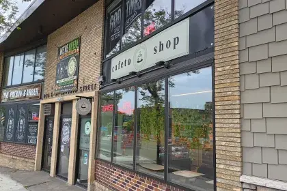 Row of East 7th Street storefronts — The Patron Barber, Good Times Tattoo Studio and Cafeto coffee shop — with a "We're Open During Construction" banner and active roadwork visible.