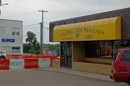 Taquería Los Paisanos storefront with a yellow awning reading "Taquería Los Paisanos / Eat In - Take Out / ¡Auténtico Sabor Mexicano!" with construction barricades nearby.