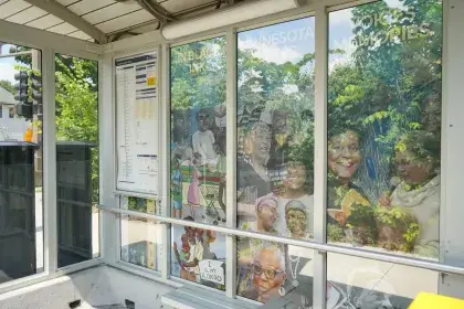 Interior view of a Selby B Line station shelter, with Rondo-themed vinyl murals titled "In Black Ink," "Minnesota Leaders" and "Voices / Memories" filling the glass panels.