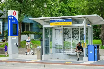 The Selby and Victoria B Line station shelter, with Rondo-themed vinyl murals on the glass panels and a person seated on the bench inside.