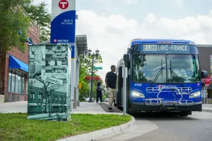 A Metro Transit B Line bus arrives at the Selby and Victoria station, with a Rondo-themed vinyl mural wrapping a utility box in the foreground.